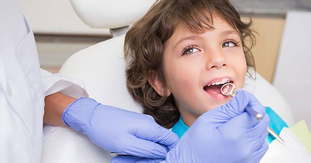 Dentist examining child's teeth, showing if the dental implants are safe for kids.