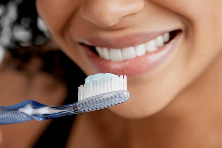 Close-up of person brushing teeth with blue-gel toothpaste on clear toothbrush.