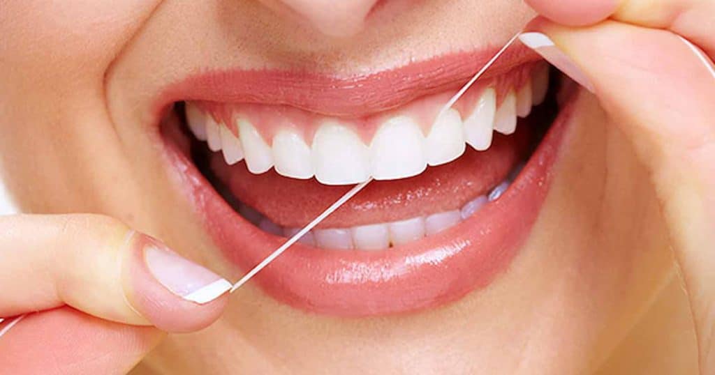 Person flossing between bright white teeth with dental floss.