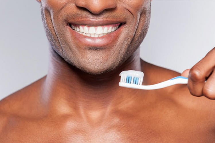 Man smiling with perfect white teeth, holding toothbrush with blue toothpaste.