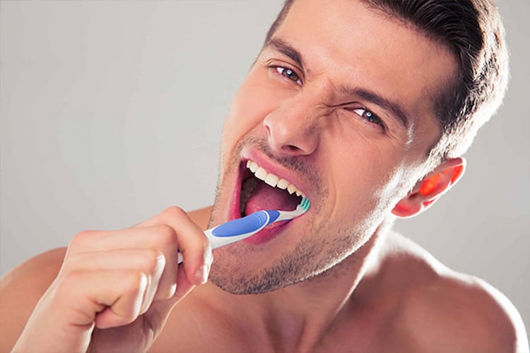 Man intensely brushing teeth with blue-and-white toothbrush.