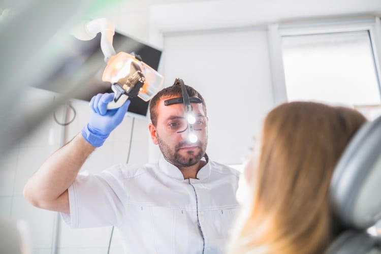 A dentist wearing full protective equipment performing a composite veneer procedure on a female patient in a modern dental clinic.