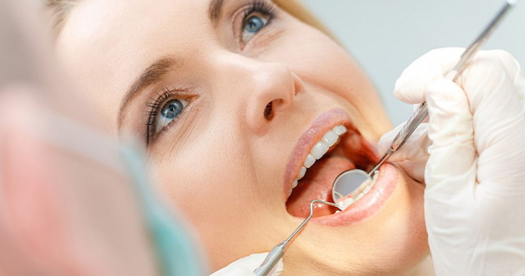 Close-up of dental mirror reflecting perfect white teeth during exam.