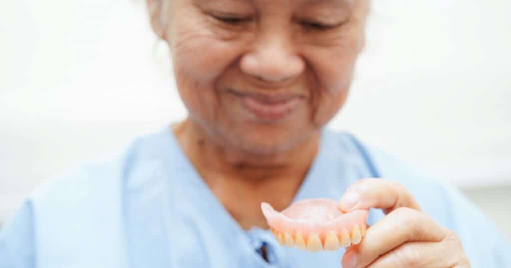 an old woman holding a Custom Denture in her hand.