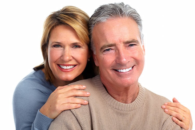 a woman hugging her man from behind, both are smiling with their custom denture.