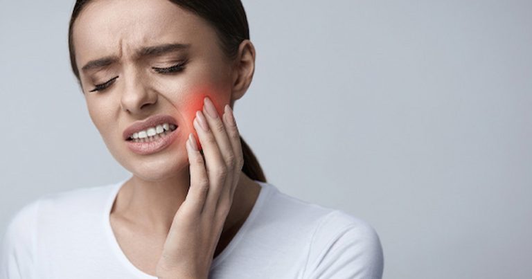 a woman is irritated by toothache, holding her hand on her cheek.