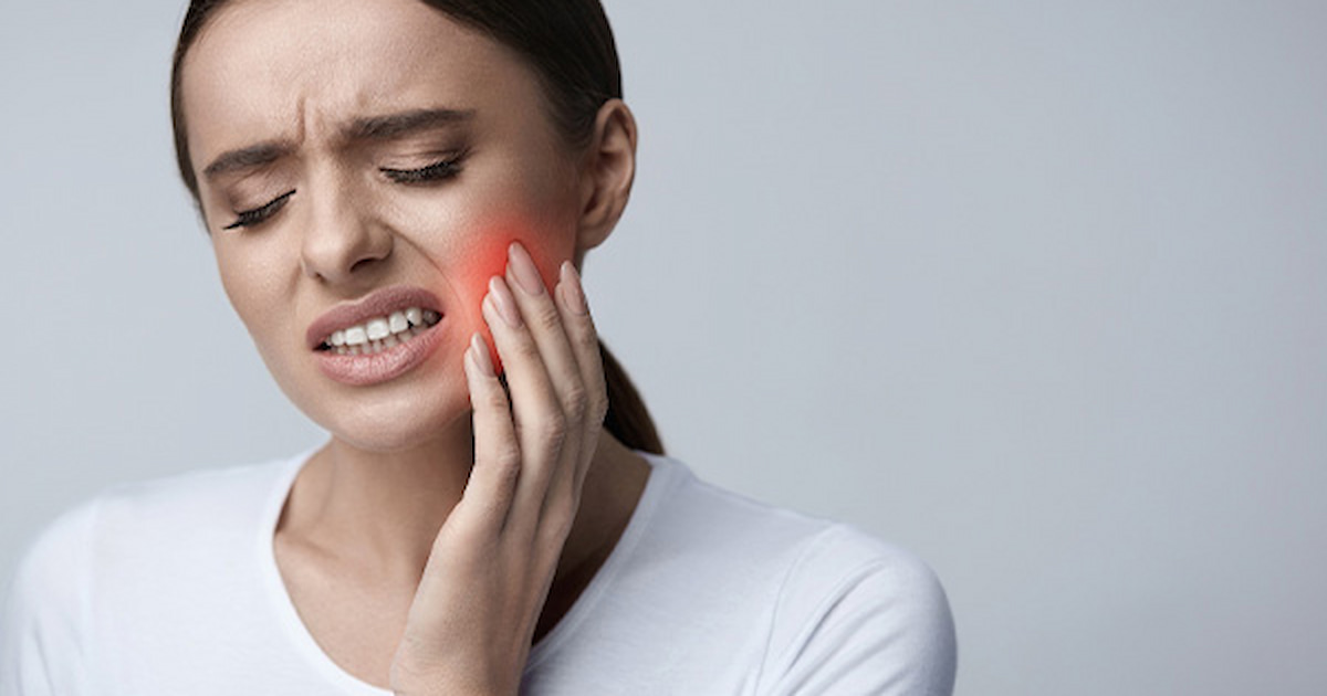 a woman is irritated by toothache, holding her hand on her cheek.