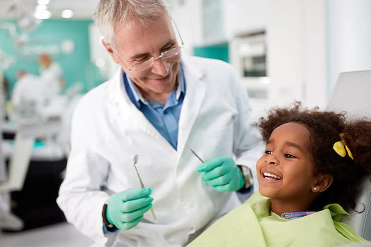Friendly dentist showing tools to happy child patient and explaining how often should you visit a dentist. 