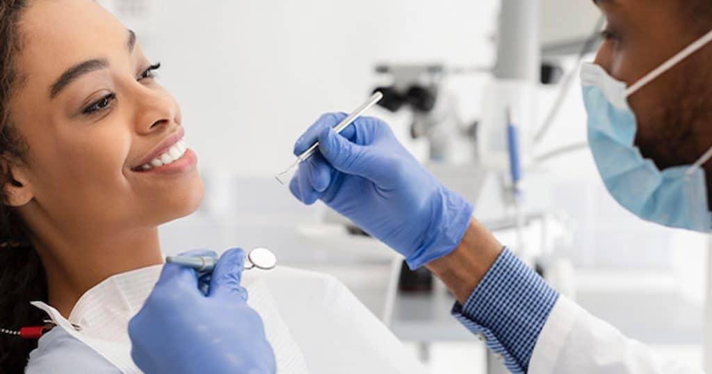 Male dentist performing oral exam on smiling female patient.