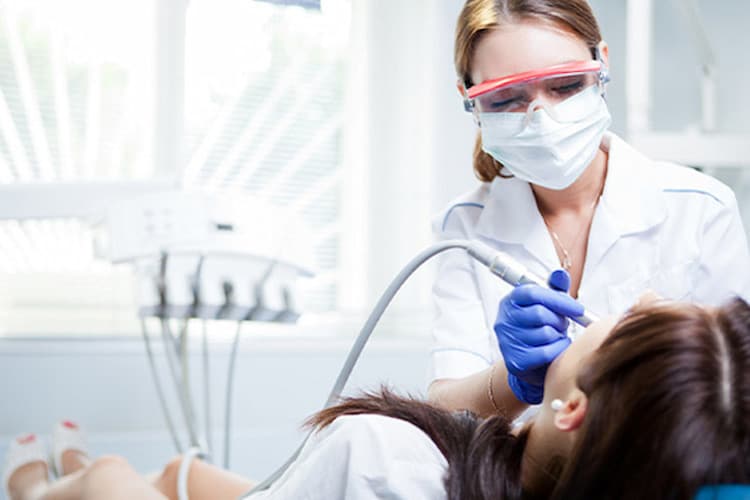 Female dentist using drill on reclined patient.