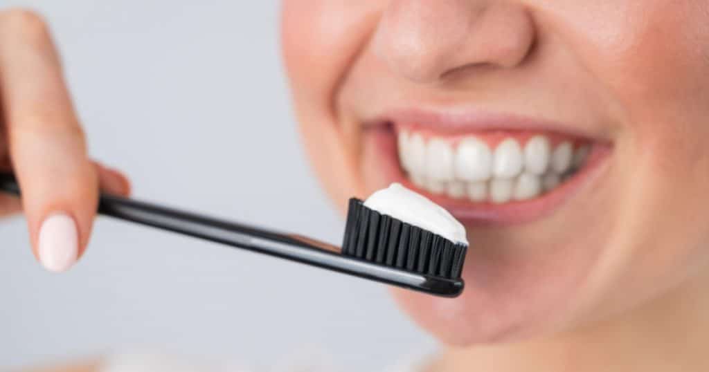 Close-up of a person brushing white veneers with a black toothbrush and white toothpaste, representing maintaining dental veneers.