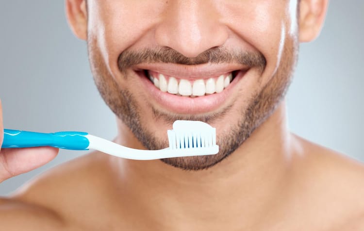 Front view of smiley man holding toothbrush with toothpaste.