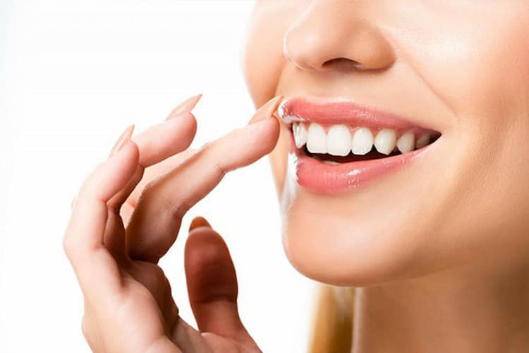 a person pointing to their bright white smile with veneers. 