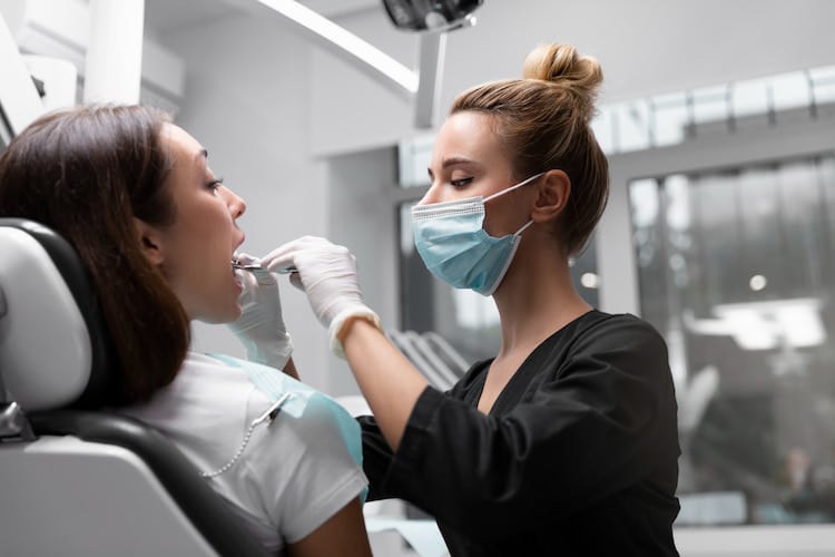 a dentist is checking a patient's teeth while wearing a mask.