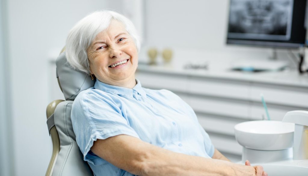 a smiling old woman is sitting on a dental chair to get her CDCP covered dental treatment.