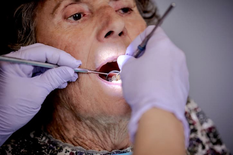 an old woman is getting dental checkup while a dentist is using their dental tools to check her dental condition.