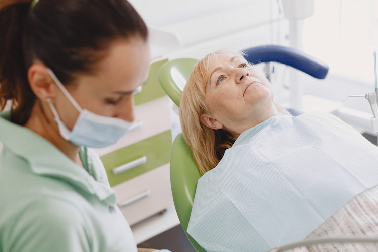 an old woman is sitting on a dental chair waiting for her treatment.