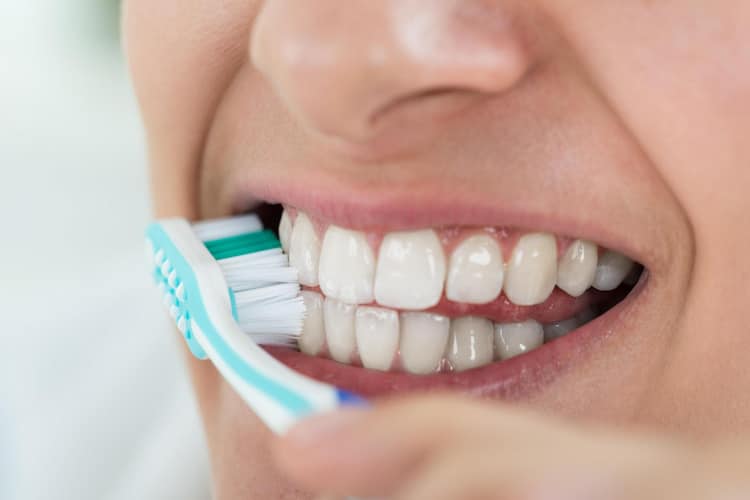 a person is carefully brushing their dental crowns to maintain the dental crown cement.