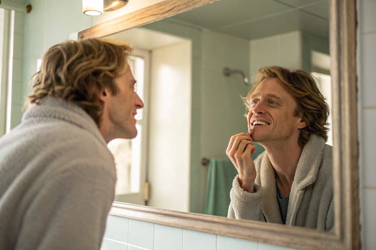 Person looking at their teeth in a bathroom mirror, inspecting a missing temporary filling