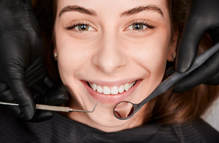 A person smiling with their mouth open during a dental procedure, with a dentist using tools, focusing on how to whiten fillings on front teeth.