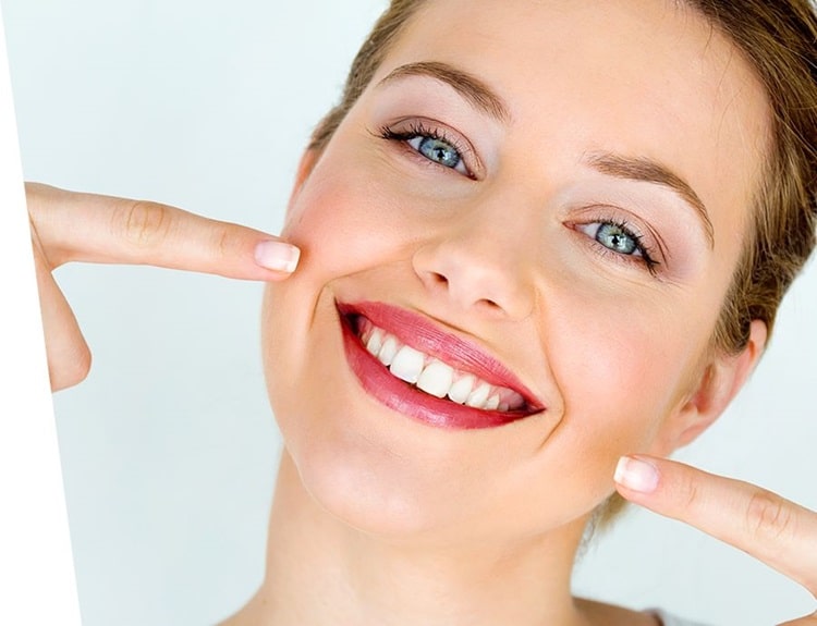 A person with a bright smile, pointing to their teeth with both hands, showcasing a healthy and whitened front tooth appearance.